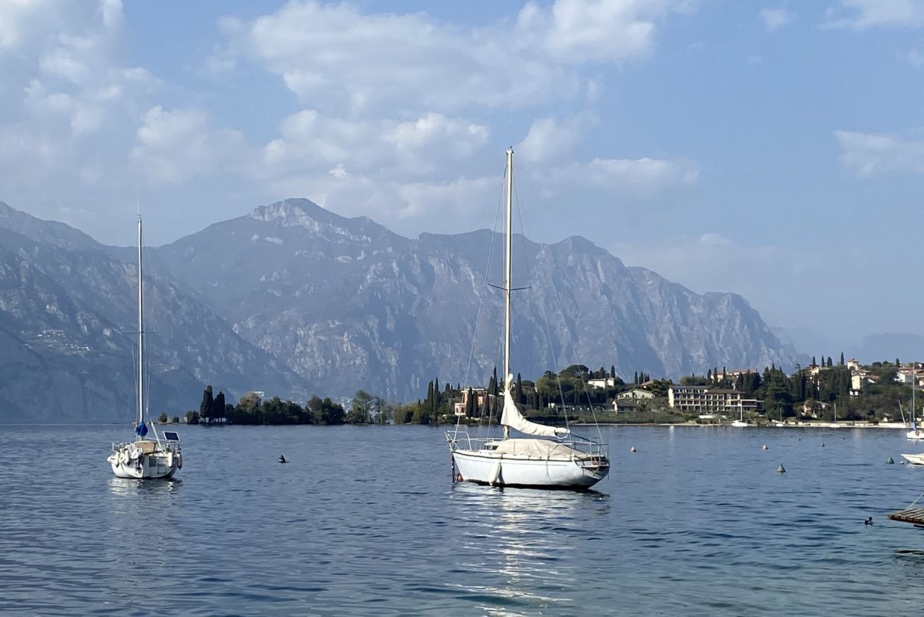 A calm lake with sailboats, mountains in the background, and a coastal town.