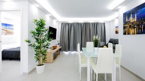 Een moderne woonkamer met een eethoek, een flatscreen-televisie, een groot raam en een potplant.
