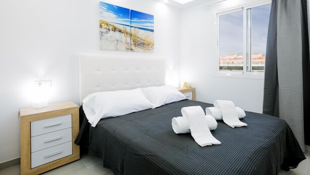 Een moderne hotelkamer met een groot bed, een nachtkastje, een bedtafel en een raam met gordijnen.