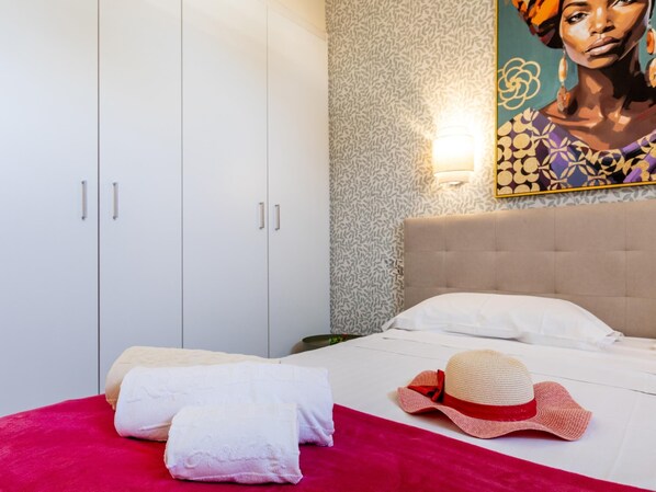 A hotel room with a bed, a headboard, a wall with a patterned wallpaper, a painting, and a hat on the bed. - Amazing Parque Santiago II 3103 (Playa de las Américas)