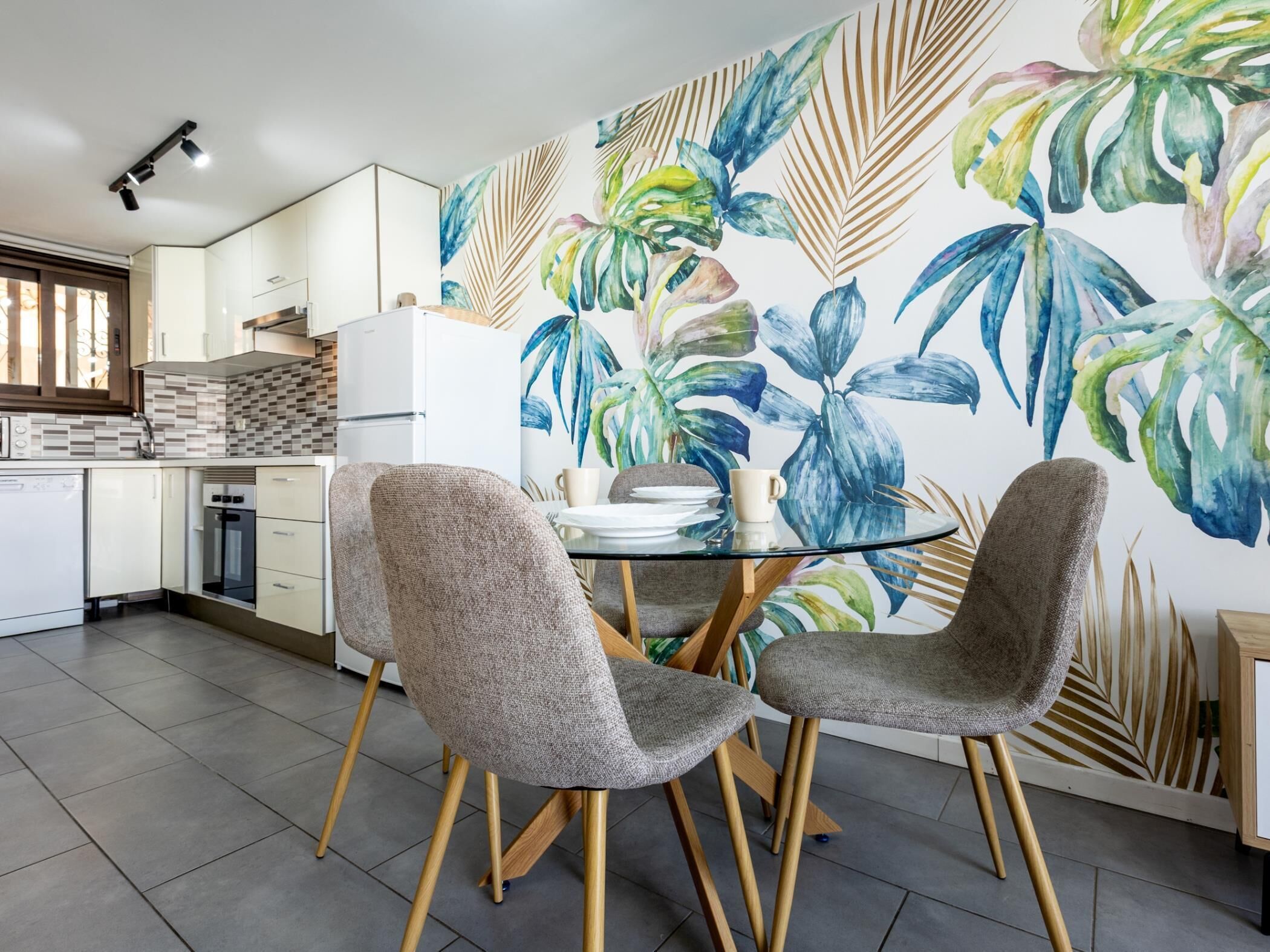 A modern kitchen with white cabinets, a tiled backsplash, and a dining area with two grey chairs and a glass table.