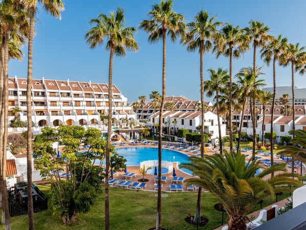 A hotel with a pool, palm trees, and a clear blue sky.