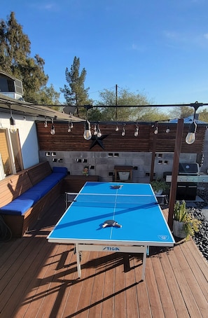 Un patio exterior con mesa de ping pong, zona de estar y una parrilla.