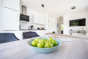 A modern living room with a dining table in the foreground, a kitchen in the background, and a sofa in the center of the room. - Villa "zweite Heimat" Exklusiv Penthouse No. 4 - Modernes Penthouse mit Sonnenterrasse und Tollem (Lohme)