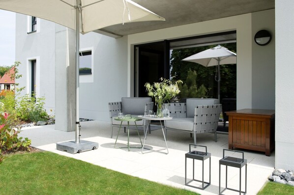 An outdoor patio with a modern seating arrangement, a table with a vase of flowers, and a wooden cabinet.