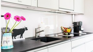 A modern kitchen with a black countertop, white cabinets, a coffee maker, and a fruit basket.