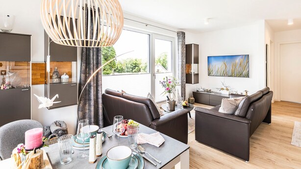 A modern living room with a dining area, large windows, and a view of greenery.