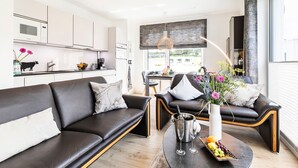 A modern living room with a sofa, a coffee table with a fruit platter, and a dining area in the background.