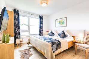 A bedroom with a bed, a desk, a chair, a rug, and a window with curtains.