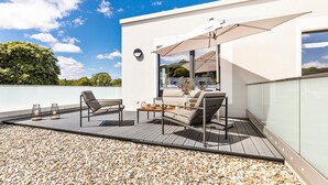A modern outdoor patio with a wooden deck, seating area, and a large umbrella.
