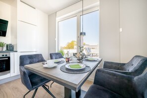 A modern dining area with a wooden table set for four, surrounded by dark upholstered chairs. A large window provides a view of the outdoors.
