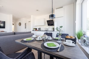 A modern living room with a dining area, grey sofa, and a kitchen in the background.