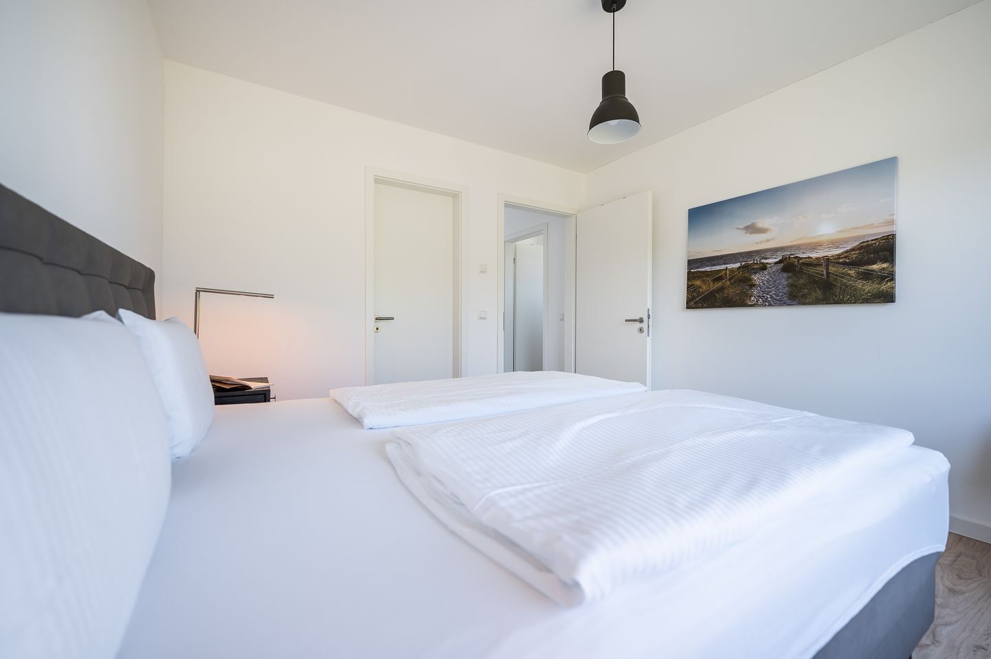 A hotel room with a bed, a nightstand, a lamp, and a painting on the wall.