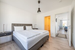 A modern bedroom with a large bed, bedside tables, a wardrobe, and a view into the living area.