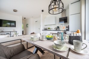 A modern kitchen with white cabinets, a dining area with a marble table, and a TV mounted on the wall.