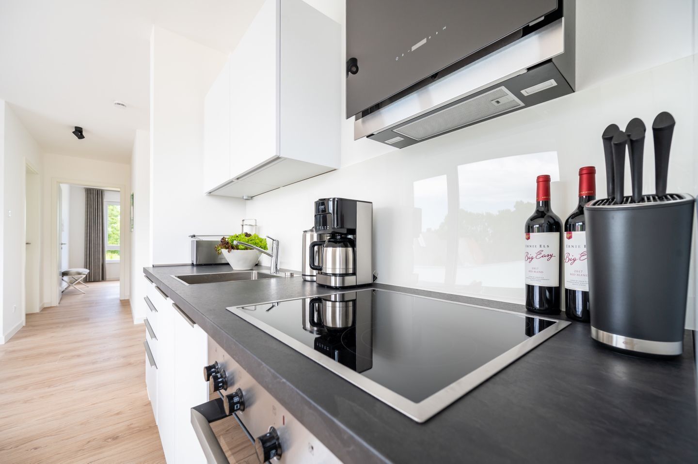A modern kitchen with a black countertop, stainless steel appliances, and wine bottles.