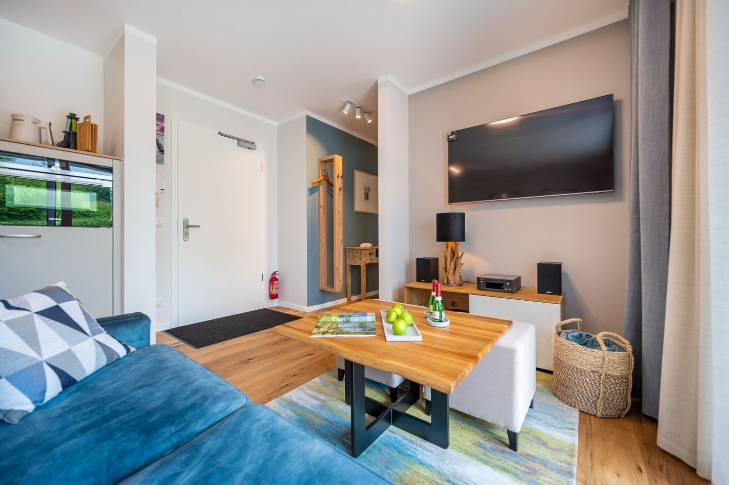 Ein modernes Wohnzimmer mit einem blauen Sofa, einem Holzesstisch und einem an der Wand montierten Flachbildfernseher.