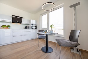 Una cocina moderna con armarios blancos, electrodomésticos de acero inoxidable y una mesa redonda con dos sillas.