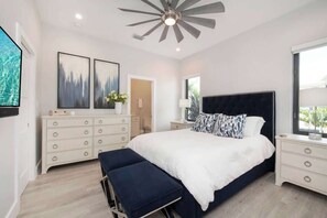 Ein modernes Schlafzimmer mit einem großen Bett, einem Deckenventilator, einer Kommode und Kunstwerken an der Wand.