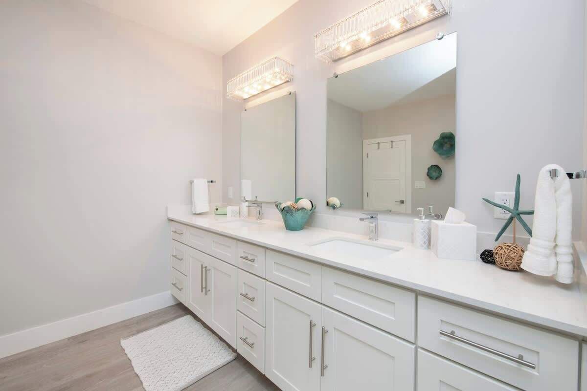 Un bagno moderno con un mobile lavabo bianco, due lavandini e uno specchio grande.