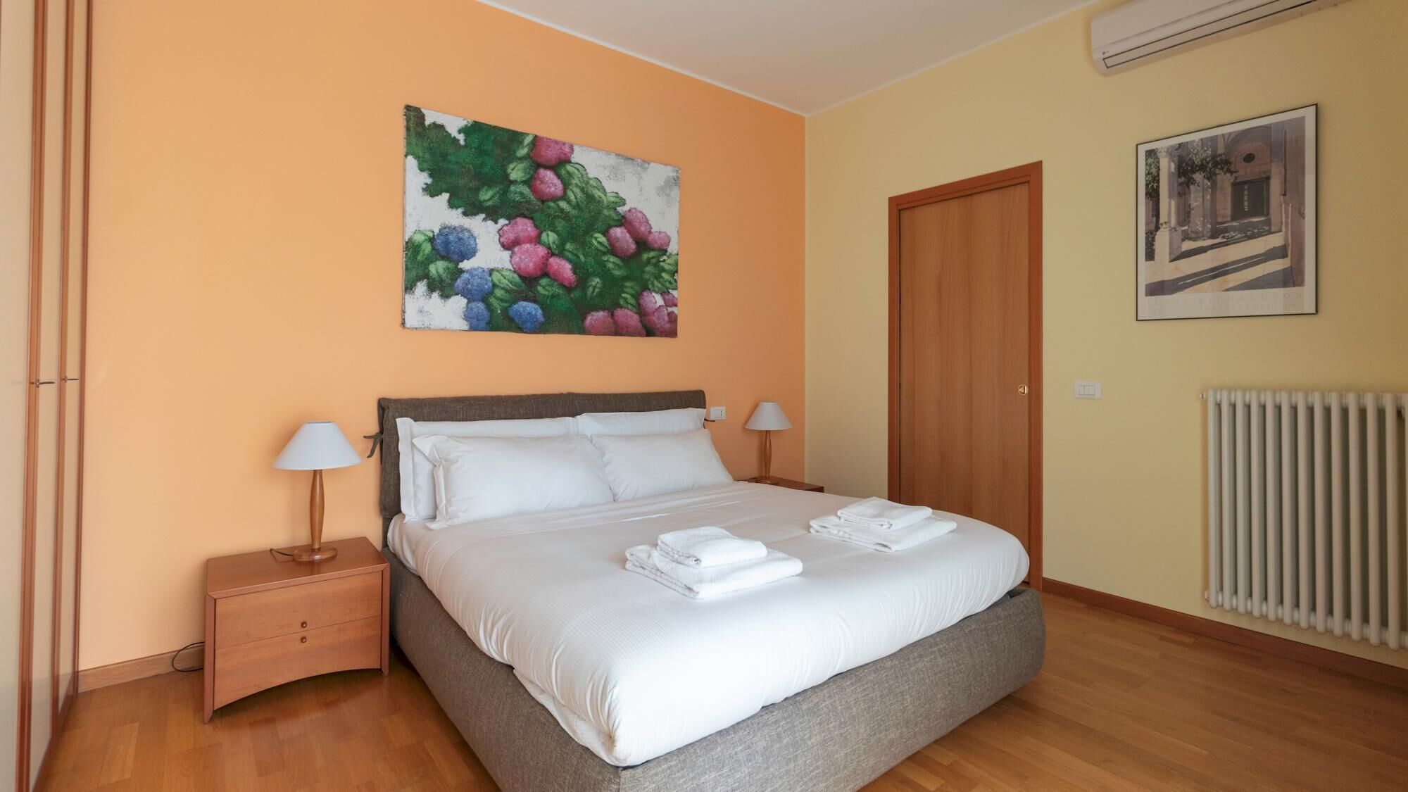 Een keurig opgemaakt slaapkamer met een bed, nachtkastjes, een schilderij en een deur.