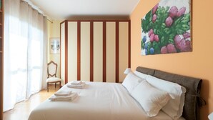 Hotellihuone, jossa on suuri sänky, tuoli, kukkakuvamaalaus ja ikkuna, jossa on verhot.
