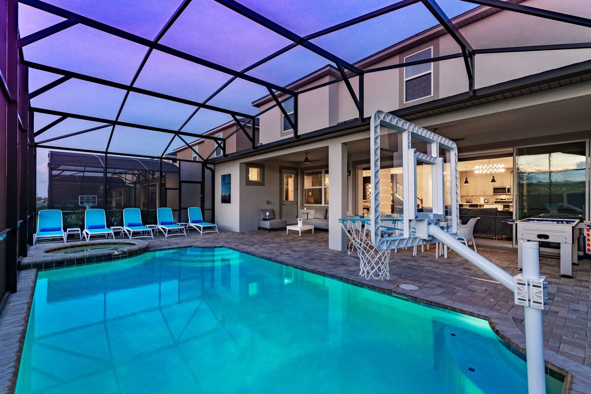 A swimming pool with lounge chairs, a sunshade, and a pool table.