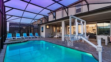 A swimming pool with lounge chairs, a sunshade, and a pool table.