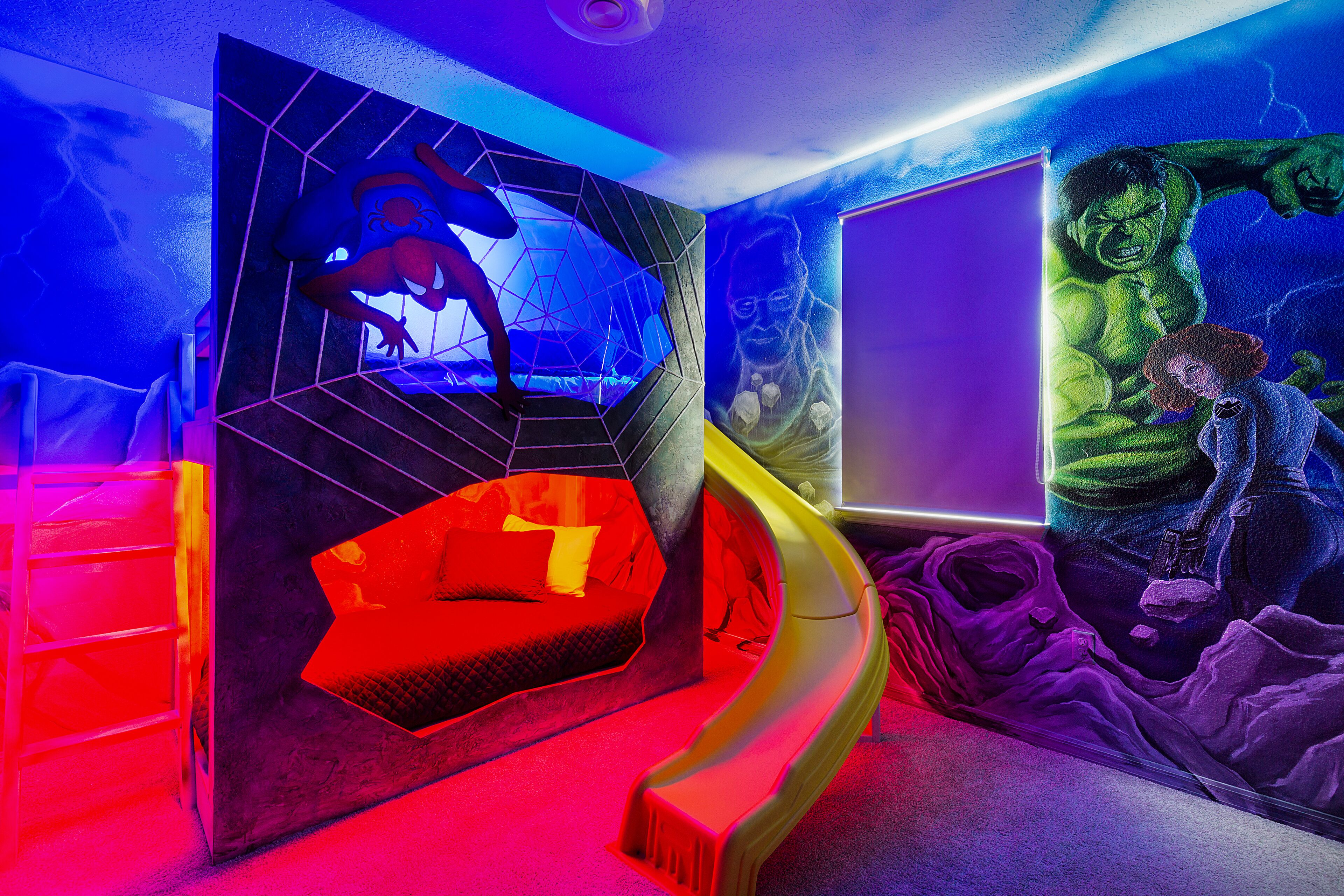 A room with a geometric wall design, a curved slide, and a mural of a green character.