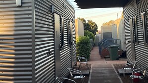 Una hilera de viviendas modulares con una galería techada y asientos al aire libre.