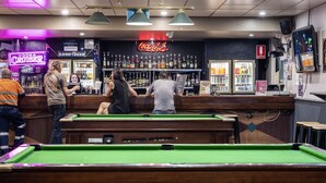 Zona de bar con mesas de billar, un cartel de Coca-Cola y varias botellas de licor.