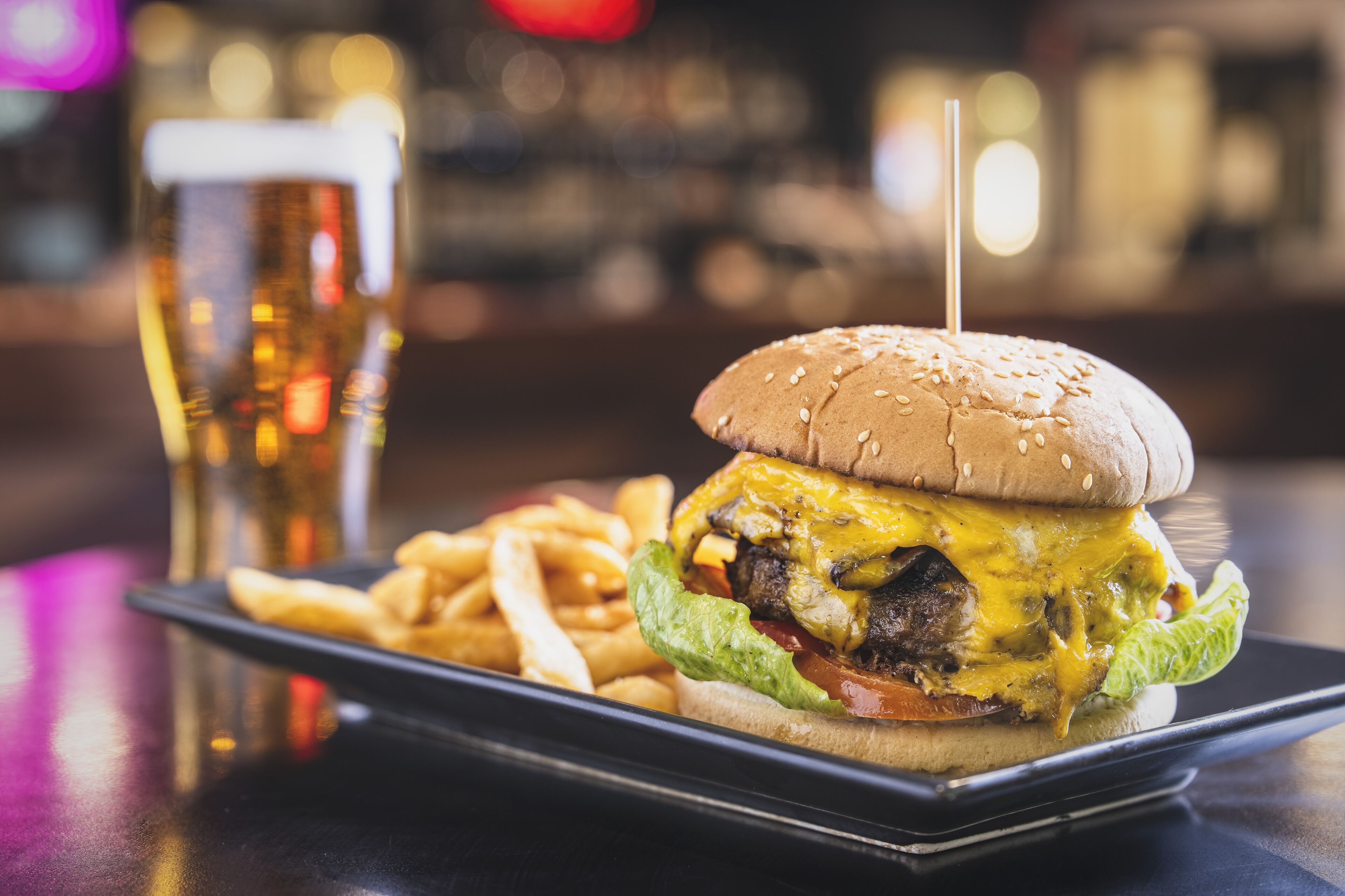 Un hamburger accompagné de frites et d’un verre de bière, le tout servi sur un plateau.