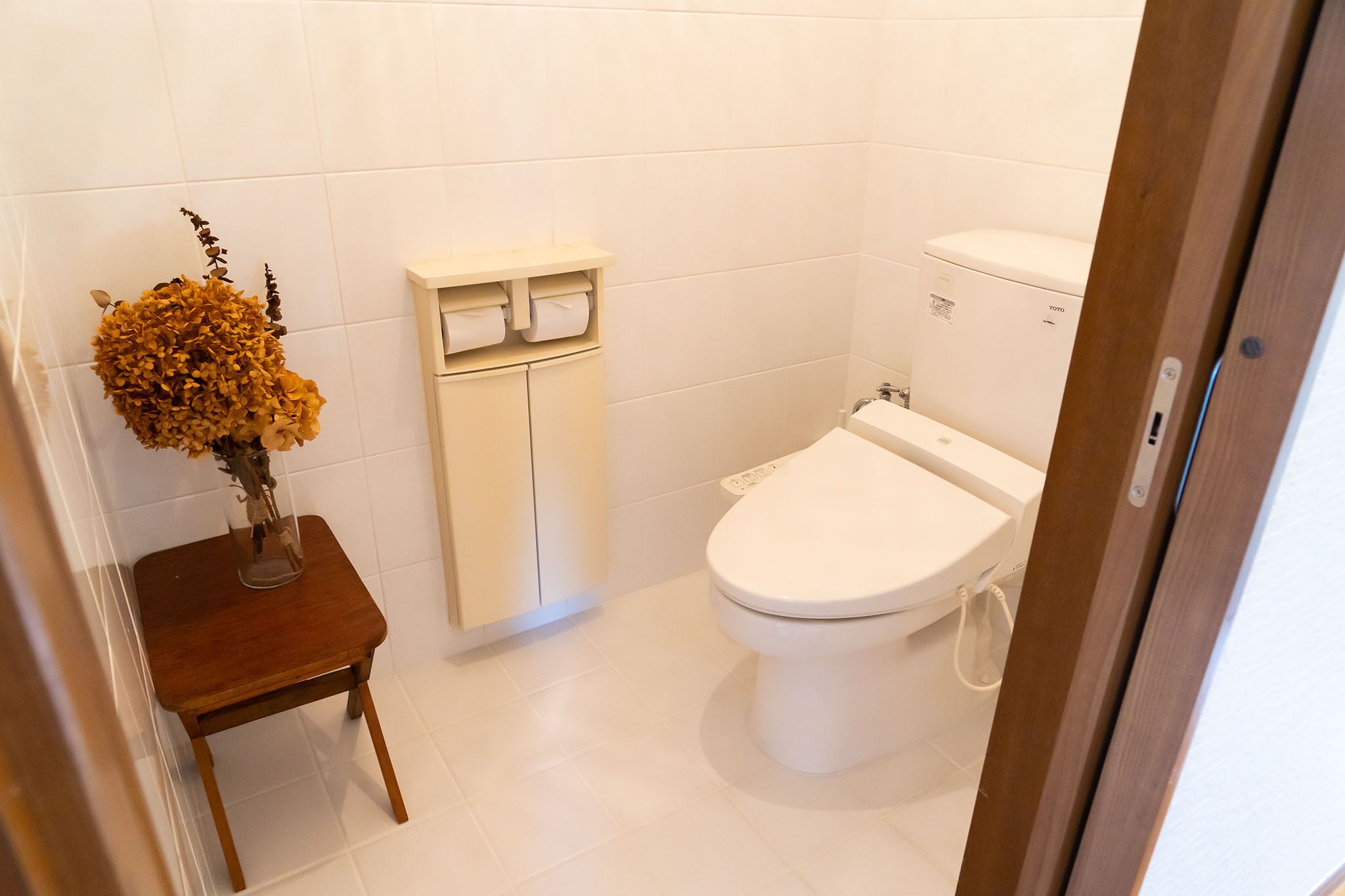 A bathroom with a toilet, a small wooden stool, and a shelf with toiletries.