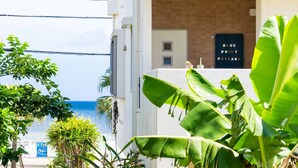 A coastal hotel with a view of the sea, a sign reading "Blue Point Okinawa," and lush tropical plants. - BLUE POINT OKINAWA (Yomitan)