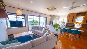 A modern living room with a sofa, dining area, and kitchen. - BLUE POINT OKINAWA (Yomitan)