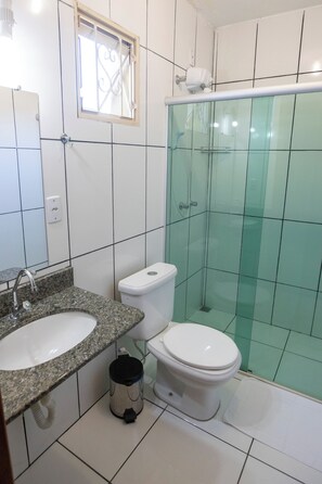 Baño con lavamanos de encimera de granito, inodoro y ducha con mampara de vidrio.
