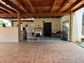 Un patio al aire libre con piso de ladrillo, vigas de techo de madera y un comedor con sillas y mesas.