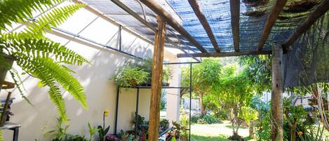 Een overdekt terras met diverse plantenpotten en een houten pergola.