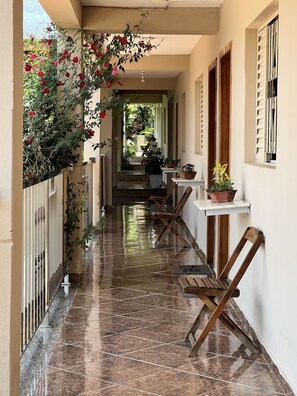 A corridor with a tiled floor, potted plants, and wooden chairs. - Hotel Pousada das Flores (Cordisburgo)