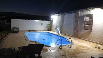 Piscina rectangular con revestimiento azul, rodeada por un patio con baldosas.