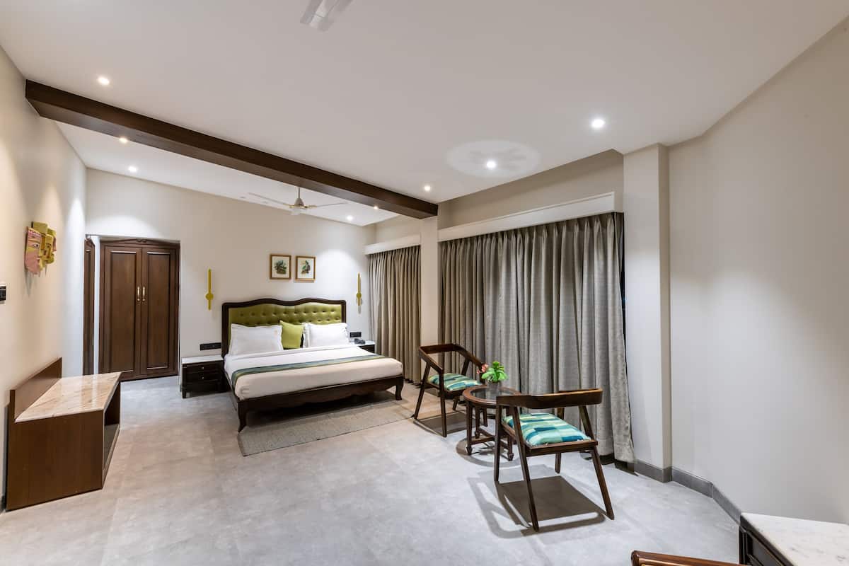 Quarto com cama, mesas de cabeceira, escrivaninha, cadeira e janela com cortinas.