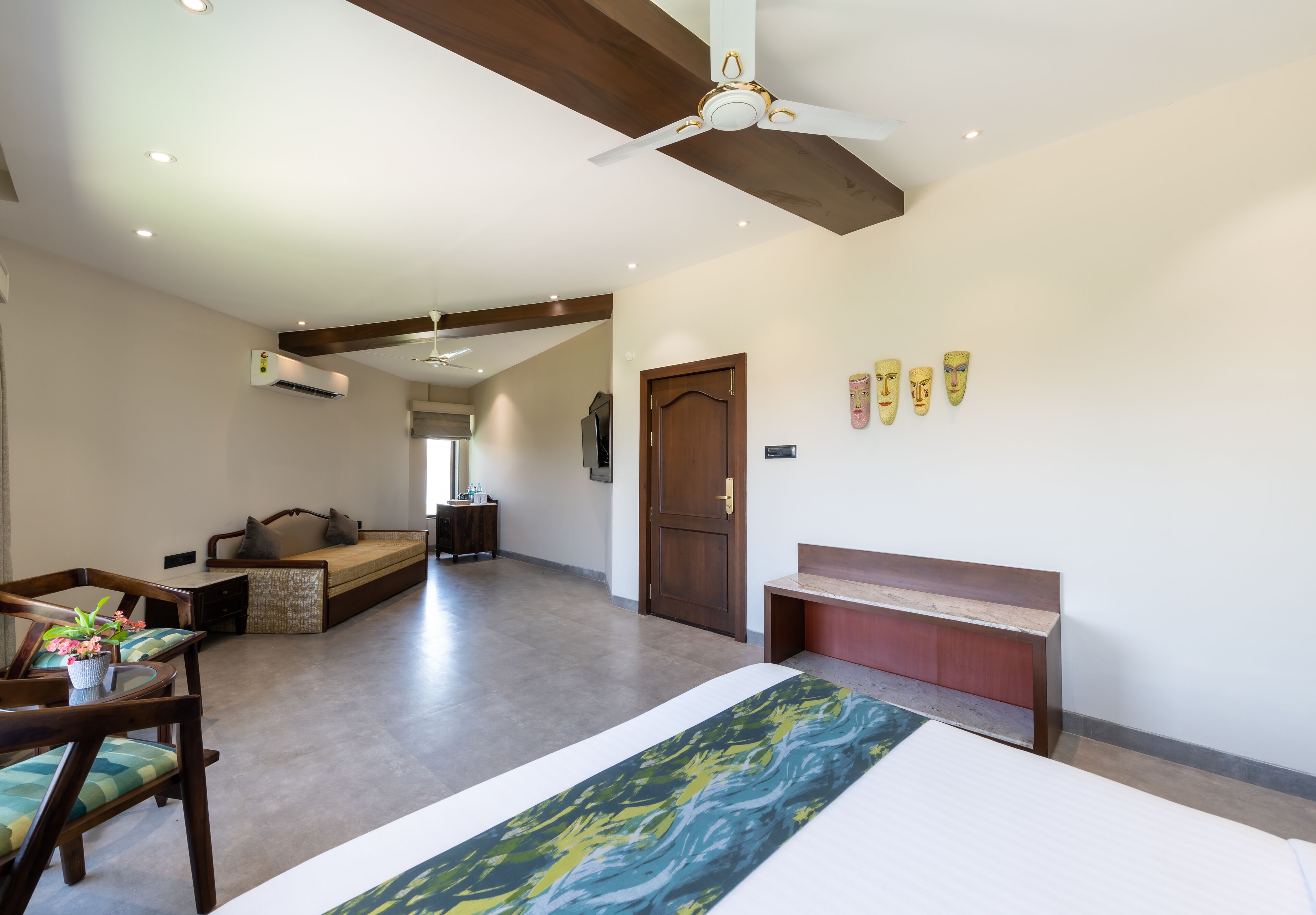 A spacious hotel room with a large bed, a wooden bench, a sofa, and a ceiling fan.