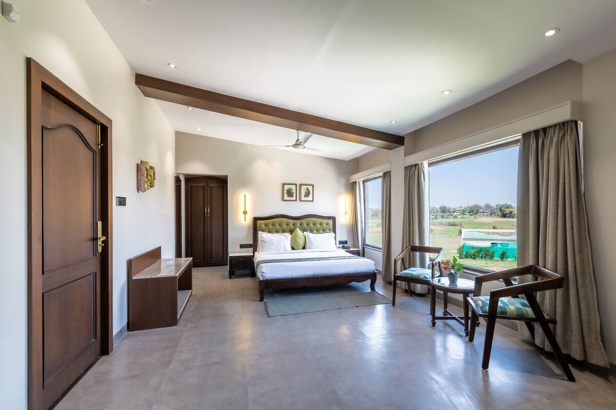 Um quarto espaçoso com uma cama grande, uma escrivaninha, uma cadeira, um guarda-roupa e vista para o exterior.