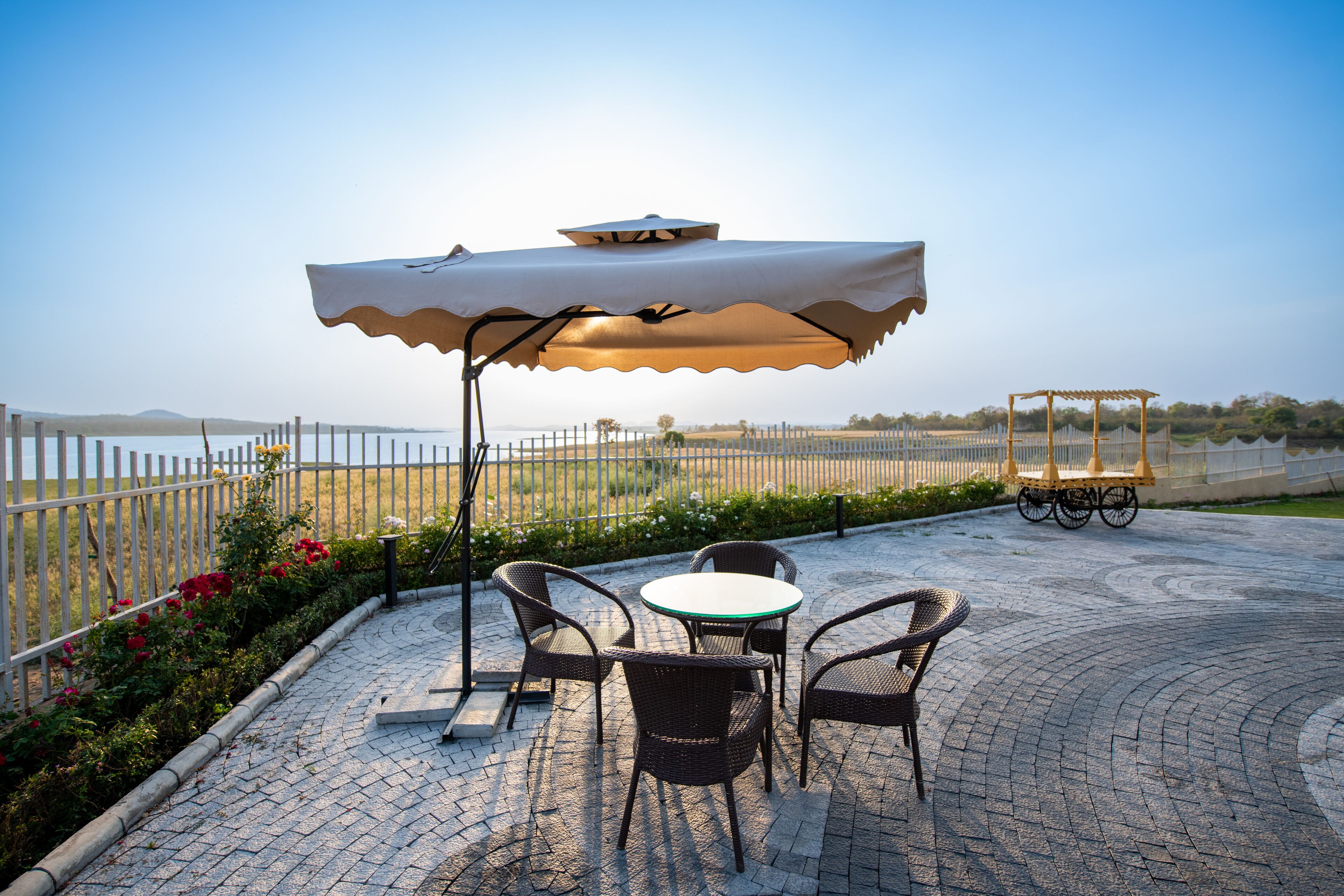 An outdoor patio with wicker chairs and a table under a large umbrella, overlooking a scenic landscape.