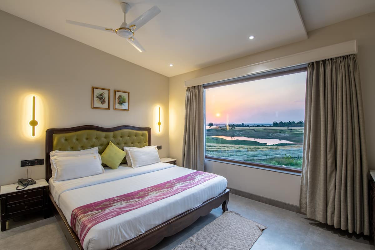 Quarto de hotel com cama grande, ventoinha no teto, mesa de cabeceira com telefone e janela com vista para a paisagem.