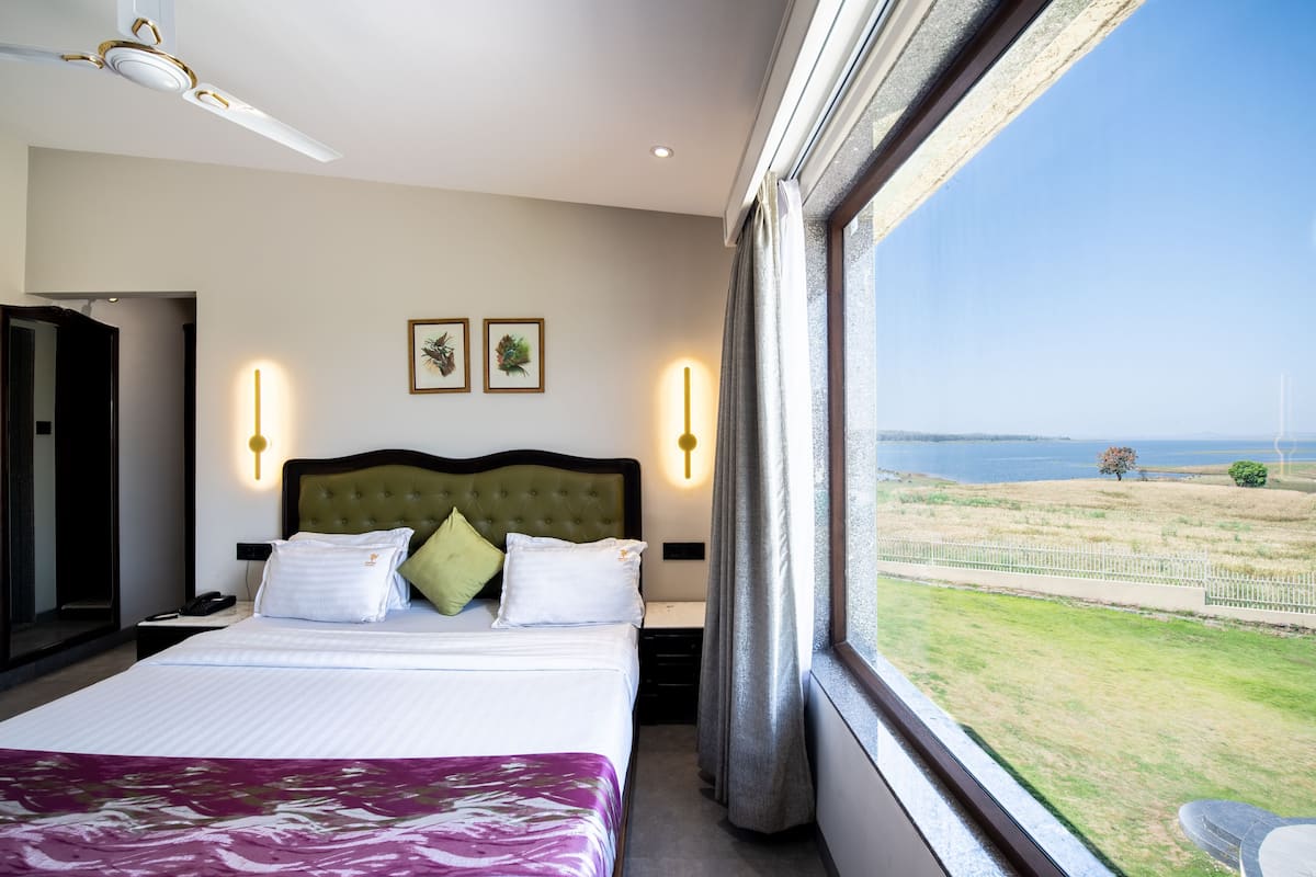 Quarto de hotel com cama, luminárias de cabeceira, mesa de cabeceira, telefone e janela com vista para o mar e paisagem.