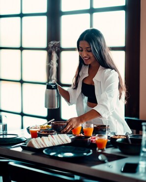 Una persona preparando una bebida con un vaporizador, rodeada de diversos alimentos y bebidas sobre una mesa.