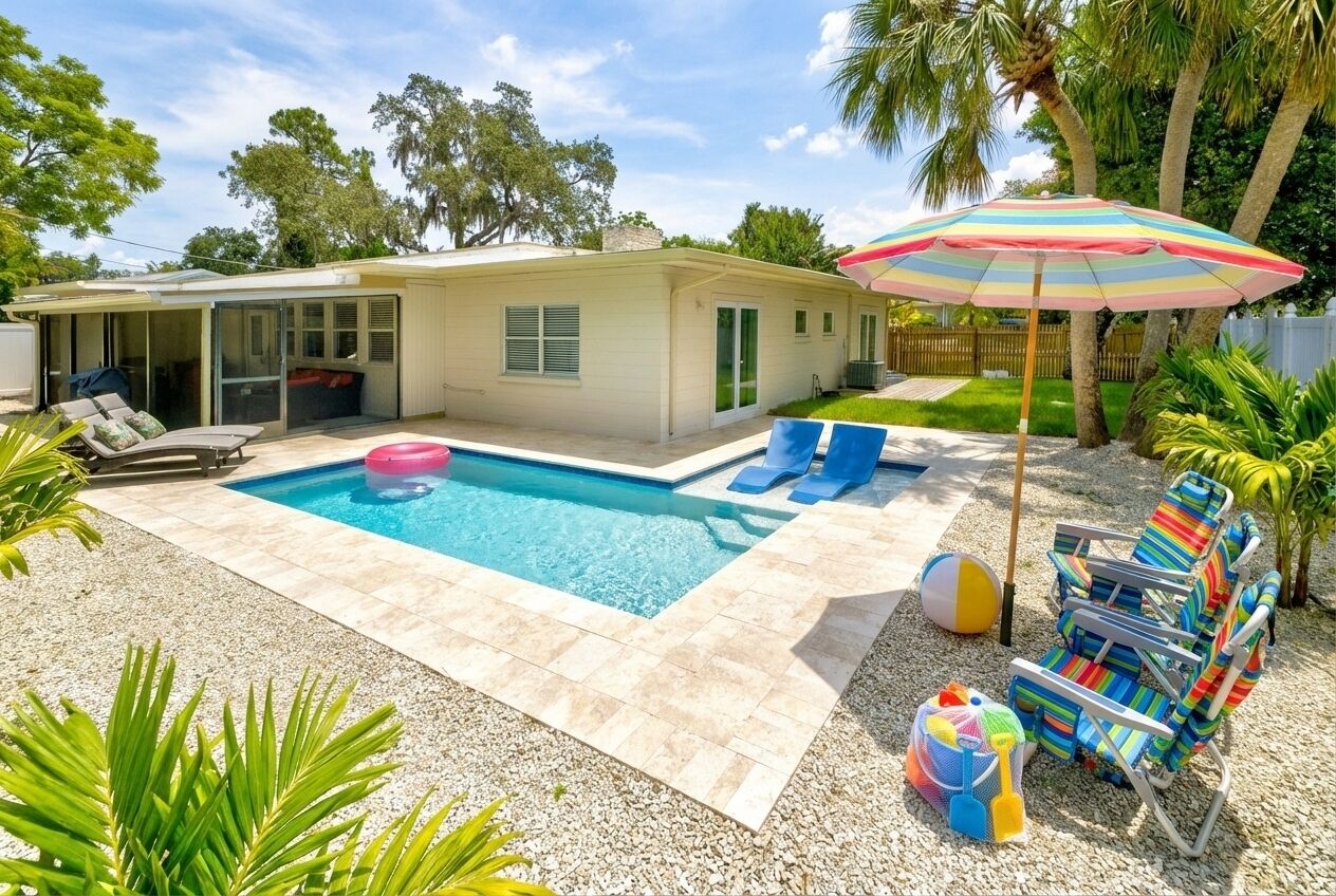 Un jardin avec une piscine, des chaises longues, un parasol coloré et une petite maison.