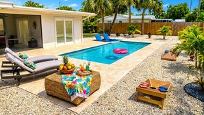 A backyard with a swimming pool, lounge chairs, a tiki bar, and palm trees. - Sun-Soaked & Heated Pool Home - Minutes to Siesta Key (Sarasota)