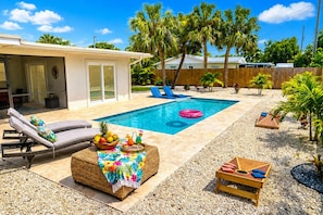 A backyard with a swimming pool, lounge chairs, a tiki bar, and palm trees.